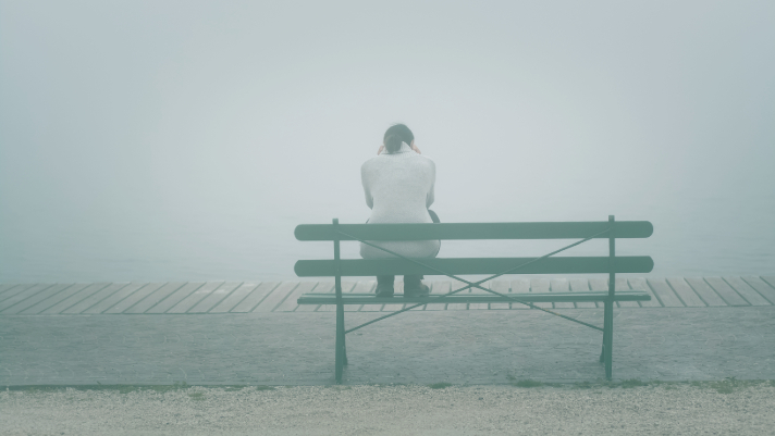 depressed woman sitting on a bench in the fog